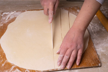 A woman cuts the dough into squares with a white ceramic knife. Plywood cutting board, wooden flour...