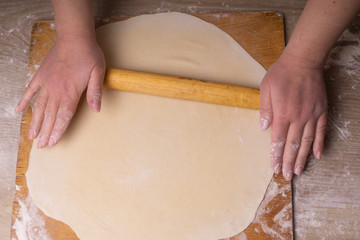 A woman rolls out the dough. Plywood cutting board, wooden flour sieve and wooden rolling pin -...