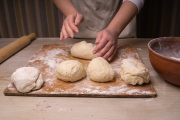 A woman kneads the dough. Plywood cutting board, wooden flour sieve and wooden rolling pin - tools for making dough.