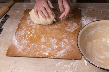 A woman kneads the dough. Plywood cutting board, wooden flour sieve and wooden rolling pin - tools...