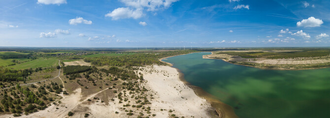 Wind wheels for green energy as a drone shot with a lake at a beautiful, clean summer day.