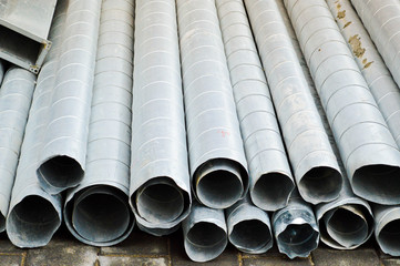 Fototapeta premium Large iron metal tin corrugated ventilation pipes of large diameter for the industrial construction of ventilation at a construction site during the repair