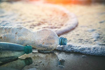 environmental ocean water pollution, used plastic bottles on sandy beach at morning or sunset light