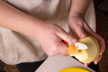 Hands of an elderly woman peeling an apple with a white ceramic knife.