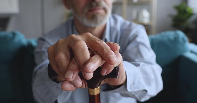 Close up older disabled sad man holding hands on cane.