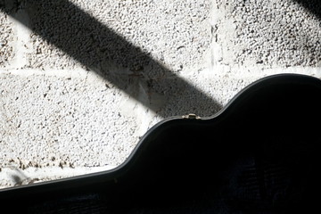 A large black guitar case rest on a concrete wall on a sunny day with shadows on the wall
