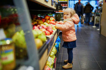 Adorable baby girl in supermarket selecting apples