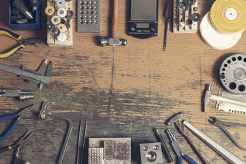 Top view of different goldsmiths tools on the jewelry workplace. Desktop for craft jewelry making with professional tools. Aerial view of tools over rustic wooden background. Poster design. - Powered by Adobe