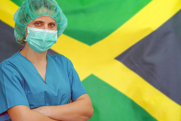 Female surgeon in mask and hat looks at the camera on the background of the Jamaica flag. Health care and medical concept. Surgery concept and fight the virus in Jamaica.