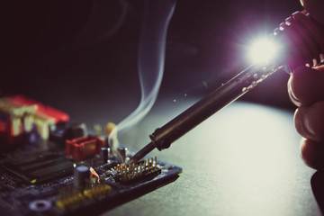 soldering iron smokes in a board chip on a dark background close-up