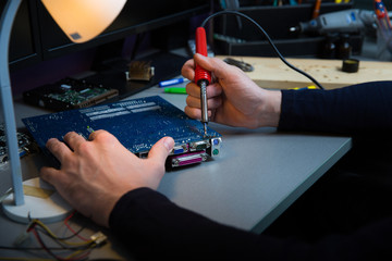 computer service worker solders a microcircuit board close up