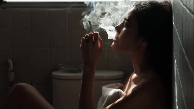 Asian woman inhaling and cigarette vaping. Female secretly smoking in bathroom at home. Concept of quit smoking and anti cigarette.