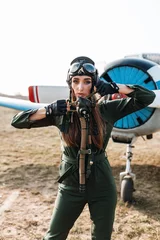 Tuinposter close-up of an aviator wearing a special headgear to protect ears with glasses, wearing a mask with oxygen to protect her lungs from discharged vodka against the backdrop of an airplane © nikitaat
