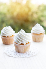 Perfect white cupcakes on a wooden table and blurred green background