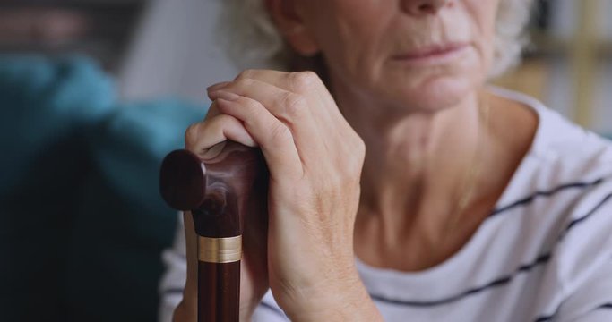 Close up upset middle aged grandma holding hands on cane.