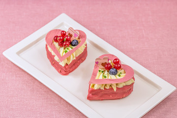 Heart-shaped cakes filled with cream and berries on the white plate at the table.
