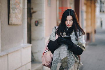 A young black-haired woman in a dark autumn coat and a wide scarf-wrap walks down the street and...