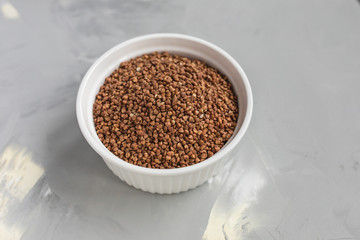 Raw buckwheat in white ceramic bowl on gray background, concept of healthy eating vegan food. Close...
