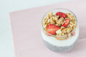 Overnight chia seed pudding with almond milk, yogurt, homemade granola, dried strawberries, almonds in glass. Superfood and vegan food concept. Copy space, selective focus, pink and white background