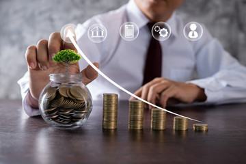 small tree growing up on jar of coin with business man or banker pressing on arrow up with...