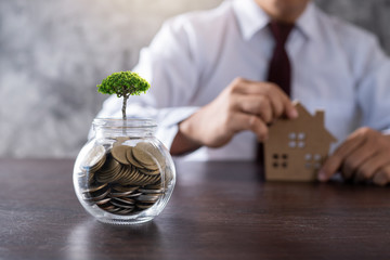 small tree growing up on jar of coin with business man or banker show real estate background
