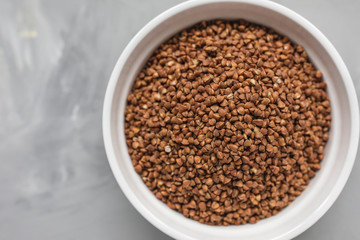 Raw buckwheat in ceramic bowl on gray background, concept of healthy eating vegan food. Close up, top view, selective focus, copy space