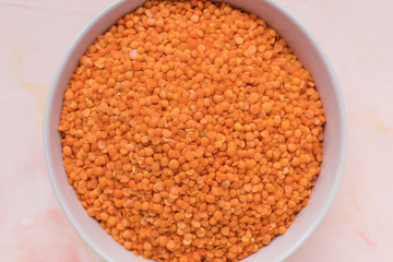 Raw red lentils in ceramic bowl on pink background, concept of healthy eating vegan food. Close up, selective focus