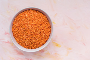 Raw red lentils in ceramic bowl on pink background, concept of healthy eating vegan food. Close up, top view, selective focus, copy space