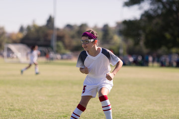 A girl with sports goggles is playing competitive soccer.