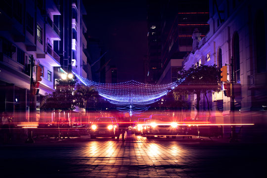 Night scene of main avenue in downtown Guayaquil, Ecuador. Light streaks from cars passing by and lights in the buildings in the foreground and background.