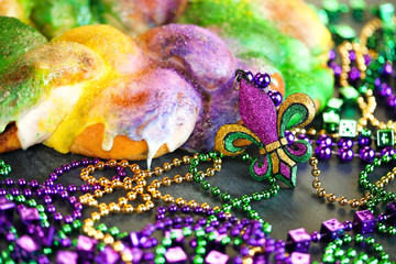 Mardi Gras king cake with yellow, green, and purple sprinkles surrounded by Mardi Gras beads and a glittering fleur de lis. © Leigh Prather