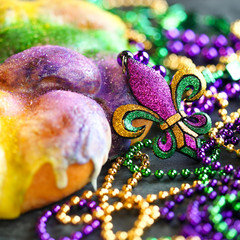 Mardi Gras king cake with yellow, green, and purple sprinkles surrounded by Mardi Gras beads and a glittering fleur de lis. © Leigh Prather