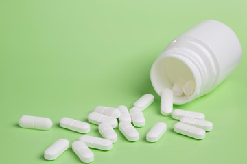 Plastic white bottles of pills on a green background of scattered white pills