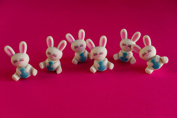 Happy, dancing white rabbit toys with Easter eggs, fun holiday art on bright pink background. 