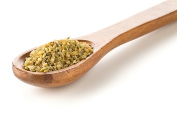 Heap of uncooked, raw freekeh or firik, roasted wheat grain, in wooden spoon over white