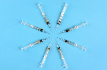Circle of eight hypodermic syringes on a blue background