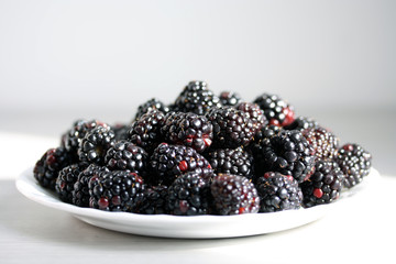 Plate with juicy ripe blackberries isolated on white