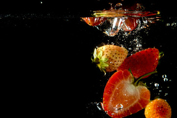 Fototapeta na wymiar strawberry falling into the water in black background