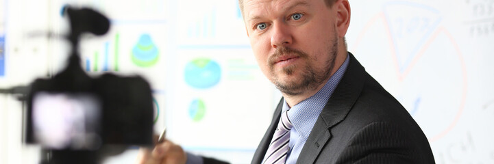 Male in suit and tie show stats graph pad making promo videoblog or photo in office camcorder to tripod portrait. Vlogger selfie solution or finance advisor management information professional concept © H_Ko