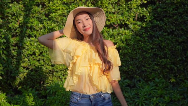 Beautiful traveler Asia young woman wearing a yellow blouse, jeans, and straw hat smile happily with a background of Green leaves wall, Happy Travel Concept.