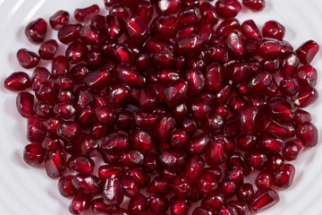 Bright red grains of pomegranate are scattered evenly on a white plate. Beautiful texture for text or decor. Studio photography under artificial lighting with two light sources.