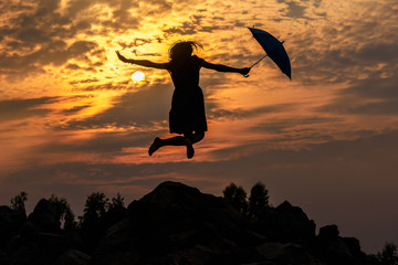 Silhouette of umbrella woman jump and sunset with big sun, landscape.