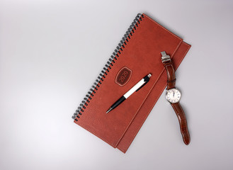 Closed notebook in leather binding with pen and clock on a gray background. Place for text.
