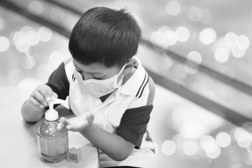 Smooth Focus, a portrait of a school boy wearing a medicine healthcare mask and applying alcohol gel to make cleaning and clear germ, bacteria in a classroom. Black and white tone.