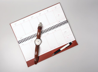 An open notebook in leather binding with a clock and pen on a gray background. Place for text.