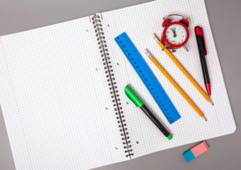 Pencils, a pen and a ruler lie on an open notebook. An alarm clock reminds of time. Office. School supplies.