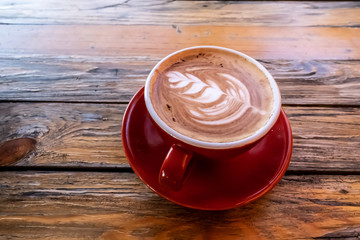 Red cup of coffee art on wooden table.