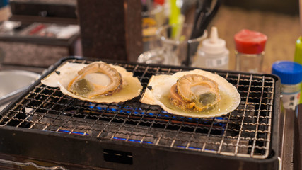A large clam shell is being grilled on a metal grill.