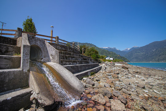 ca&iacute;da de agua por desague con fondo de cielo azul y piedras