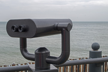 Shiny black binoculars on a swivel hinge on observation deck on sea embankment, directed to the...